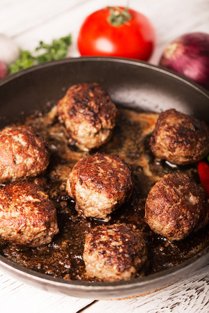 Fried meatballs (cutlets) on the pan and vegetables on the wooden tableの写真素材