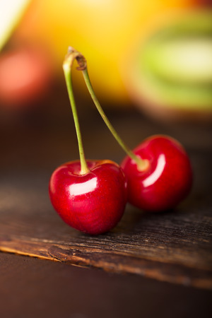 Two cherries an other fruits on a wooden tableの写真素材