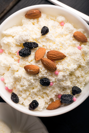 Cottage cheese with almond and raisins in a white bowlの写真素材