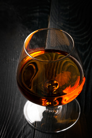 Glass of cognac on the dark wooden table. Black backgroundの写真素材