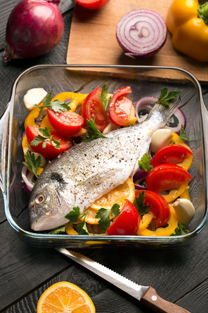 Uncooked dorado or sea bass fish with vegetables, herbs and spicesの写真素材