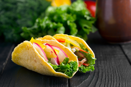 Taco with fresh vegetables and meat on a black wooden surfaceの写真素材