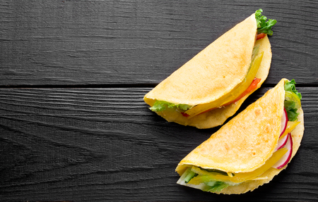 Taco with fresh vegetables and meat on a black wooden surfaceの写真素材