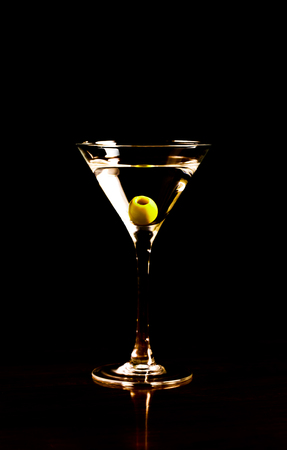 Glass of martini cocktail on a black background. Green olive inside the glassの写真素材