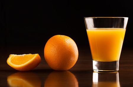 A glass of chilled orange juice and oranges on a black backgroundの写真素材