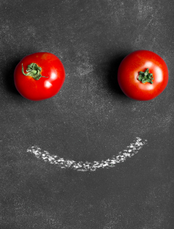 Two red tomatoes on the black chalkboard (top view)の写真素材