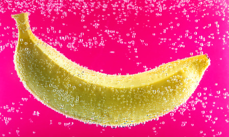 Yellow banana surrounded by water bubbles on the red background