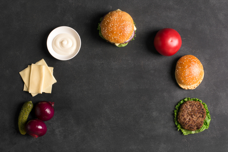 Beef burger with lettuce and sauce on the black chalkboard. Ingredients of popular takeaway foodの写真素材