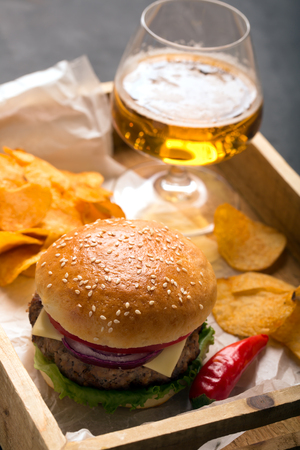 Beef burger with lettuce and beef cutlet. Potato chips and glass of beerの写真素材