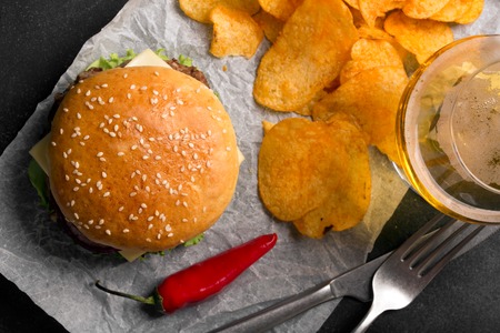 Beef burger with lettuce and minced meat cutlet. Potato chips and glass of beerの写真素材