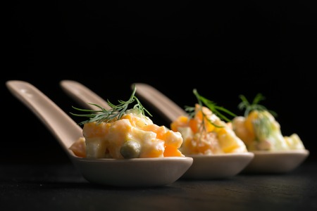 Traditional Russian salad olivie with boiled vegetables and mayonnaise on a black background. Portion Control spoonの写真素材