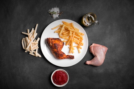 Fried Chicken leg and french fries with sauce on a black chalkboard. Top viewの写真素材