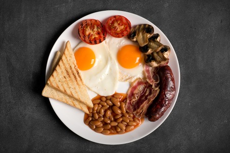 English breakfast prepared with two fried eggs, beans in tomato sauce, grilled tomatoes, mushrooms,...