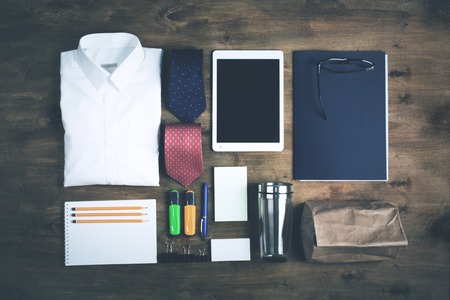 Business objects on the desk,including digital tablet, shirt, ties, lunch box, paper and pencils, top view, toned photoの写真素材