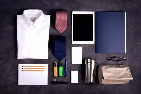 Business objects on the desk,including digital tablet, shirt, ties, lunch box, paper and pencils, top view, black chalkboard, toned imageの写真素材