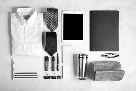 Business objects on the desk,including digital tablet, shirt, ties, lunch box, paper and pencils, top view.White background, black and white imageの写真素材