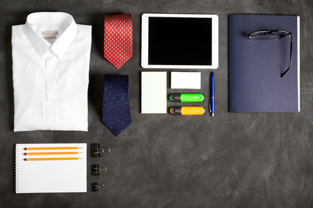 Business objects on the desk,including digital tablet, shirt, ties, lunch box, paper and pencils, top view with copy space. Black chalkboard as backgroundの写真素材