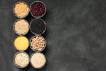 A selection of various colorful cereal on a black chalkboard in bowls. Copy space for textの写真素材