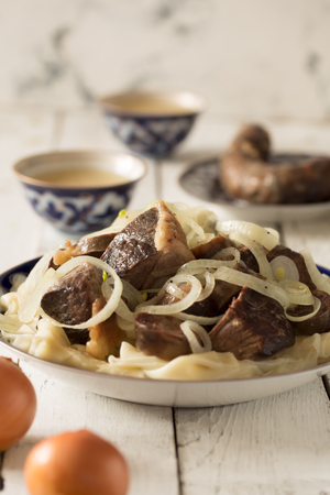 National Kazakh dish - Beshbarmak prepared with meat and pasta on the white wooden tableの写真素材