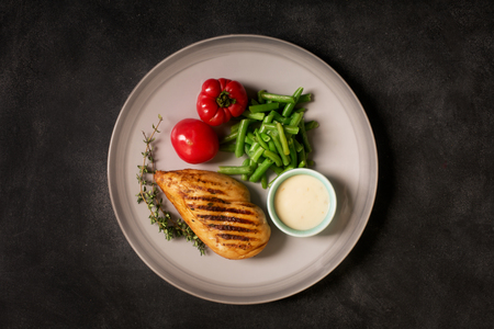 Marinated grilled healthy chicken breast served with green beans and, white sauce and fresh tomatoes on a black chalkboard, top viewの写真素材