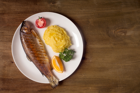 Grilled whole trout, potato, lemon and garlic, close up. Wooden backgroundの写真素材