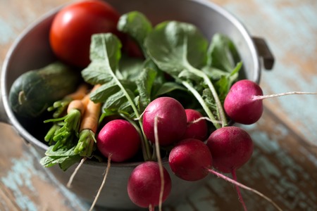 Fresh farm vegetables in bowl. Radish, carrot, cucumber and tomato on old wooden rustic backgroundの写真素材