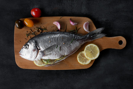 Mediterranean fish - dorado and vegetables on the cutting board. Top view.の写真素材