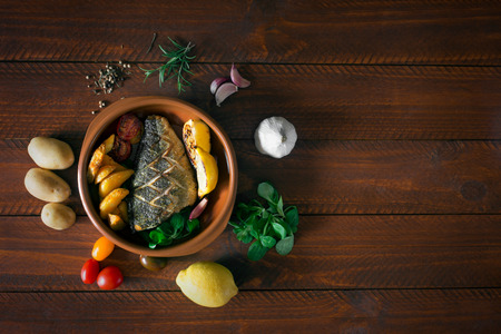 Baked dorado with fresh salad and vegetables. Top view. Brown wooden tableの写真素材