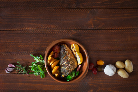 Baked dorado with fresh salad and vegetables. Top view. Brown wooden tableの写真素材