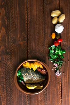 Baked dorado with fresh salad and vegetables. Top view. Brown wooden tableの写真素材
