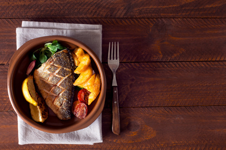 Baked dorado with fresh salad and vegetables. Top view. Brown wooden tableの写真素材