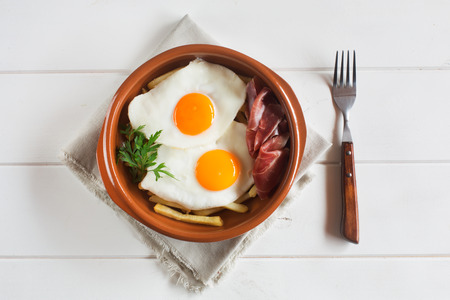 Traditional lunch - fried eggs with french fries, cured pork slices jamon on the white wooden tableの写真素材