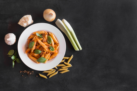 Italian Penne pasta with Bolognese sauce and ingredients. Top view on the black backgroundの写真素材