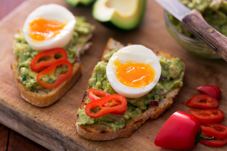 Healthy breakfast- sandwich prepared with guacamole, pepper and boiled chicken egg on the wooden chalkboardの写真素材