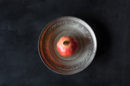 Ripe pomegranate on a metallic plate on a dark background. Top viewの写真素材