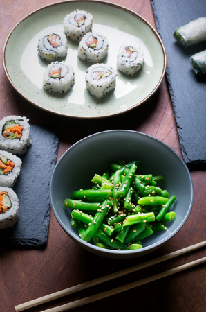 Traditional japanese and chinese food. Steamed green beans and sushi rolls on a brown wooden tableの写真素材