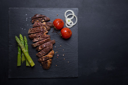 Grilled tasty and juicy beef steak on a black background with tomatoes, asparagus and onion, pepper and saltの写真素材