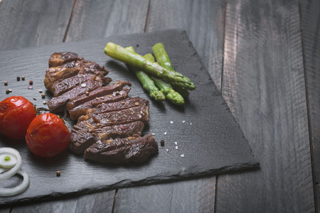 Grilled tasty and juice beef steak on a black background, vegetables, toomatoes, onions and asparagus, with pepper and saltの写真素材