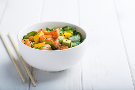 Hawaiian Poke salad with salmon, avocado and vegetables in a bowl on a white wooden rustic background with copy space, vegetables and chopsticks. Horizontalの写真素材