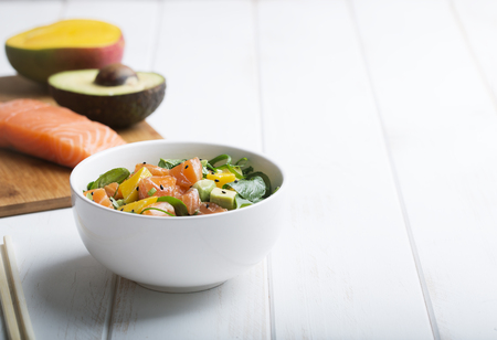 Hawaiian Poke salad with salmon, avocado and vegetables in a bowl on a white wooden rustic background with copy space, vegetables and chopsticksの写真素材
