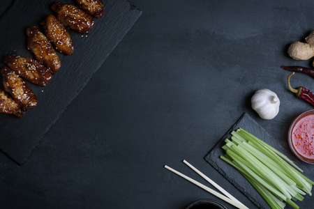 Traditional Asian chicken wings in sweet sauce with ingredients on the black tableの写真素材
