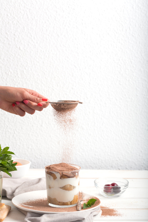 Woman powders cocoa powder on tiramisuの写真素材