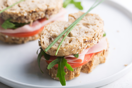 Homemade sandwiches with ham, tomatoes and fresh vegetables salad sprinkled with olive oil. Food on the white stylish plateの写真素材