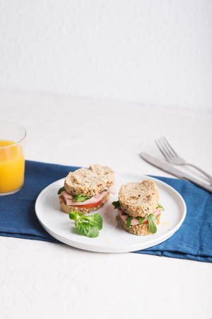 Homemade sandwiches with ham, tomatoes and fresh vegetables salad sprinkled with olive oil. Food on the white stylish plateの写真素材