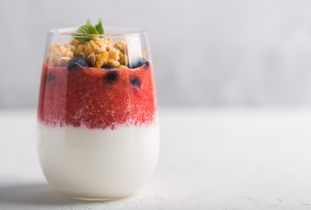 Glass of yogurt or panna cotta with strawberry mousse and granola on a whiteの写真素材