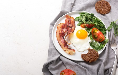 Photo of hearty high protein english style breakfast with egg, fried bacon and arugula on the plateの写真素材