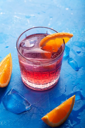 Fresh ice tea summer cocktail with orange and ice in glass on blueの写真素材