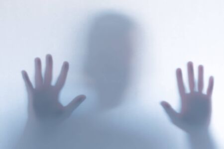 Blurred scary ghost silhouette behind a white glass background. Horizontal orientation