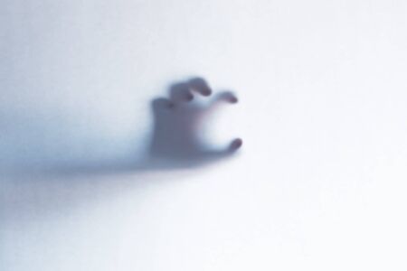 Blurred scary ghost hands behind a white glass background. Horizontal orientation
