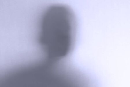 Blurred scary ghost face behind a white glass background. Horizontal orientation
